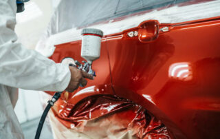 Man With Protective Clothes And Mask Painting Car Using Spray Compressor.