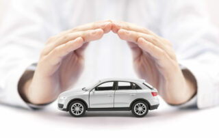 Car Insurance. Small Silver Car Covered By Hands.